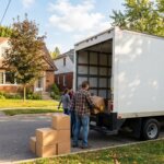 Donation truck parked outside suburban house with volunteer loading boxes