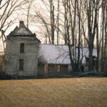 Old run-down farmhouse with peeling paint and weathered siding sitting in an open field.