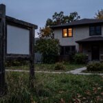 A weathered blank real estate sign standing in an overgrown front lawn at dusk outside a Winnipeg two-storey home, representing a listing that expired without selling