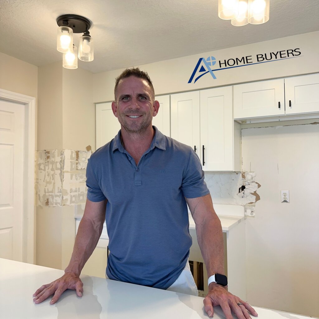 Owner of A+ Home Buyers, Mike Youngblood, posing for picture in kitchen of house that being remodeled and wearing a blue polo shirt. 