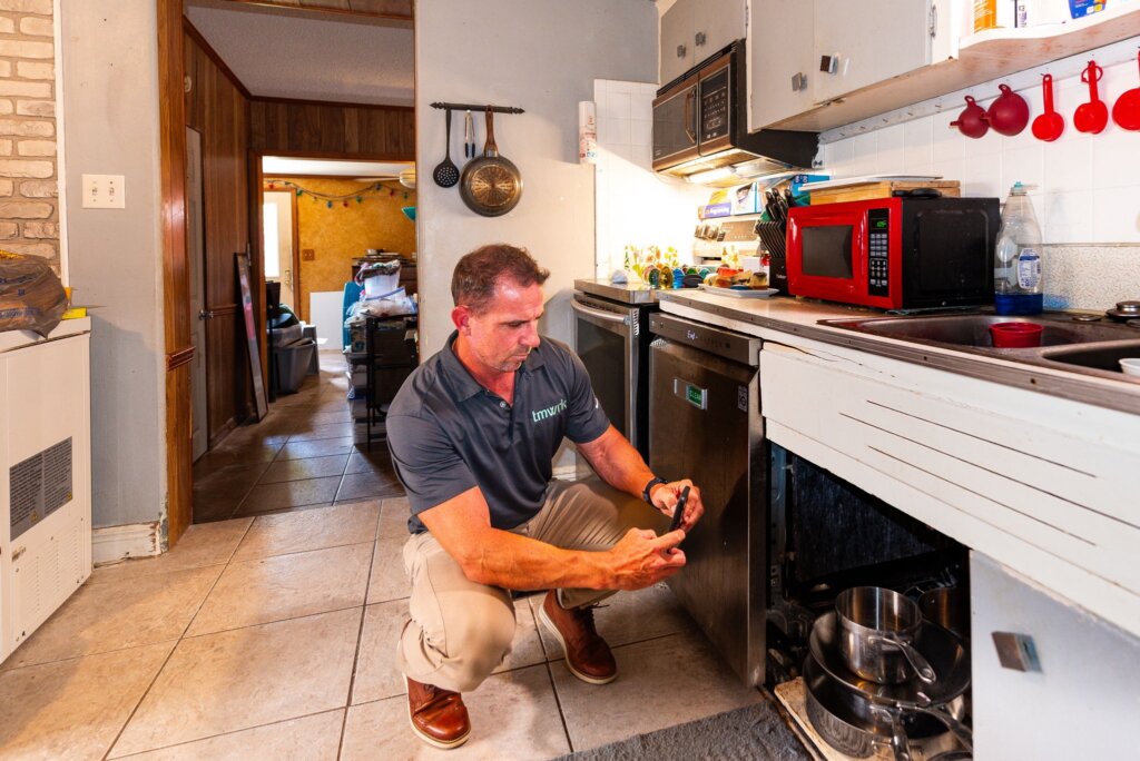 Picture of Mike Youngblood squatting on the ground taking a picture underneath the sink while inspecting a home.
