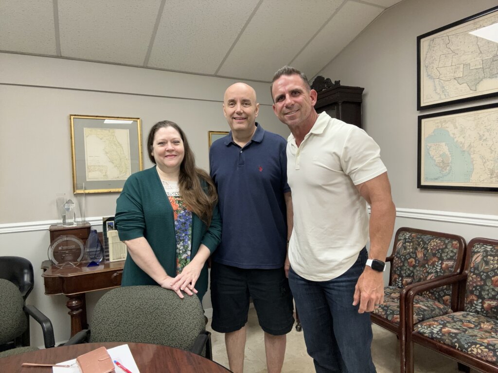 Owner of A+ Home Buyers, Mike Youngblood, posing for a picture with Terry and Del after the just signed closing docs at Peer Title in Tampa. Mike is wearing a white polo shirt, Del is wearing a blue polo shirt, and Terry has on a green dress. They all look very happy the deal got closed quickly and hassle free.