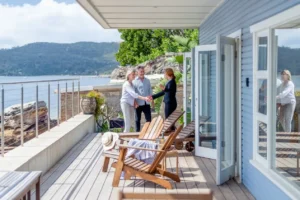 Three individuals shaking hands on a sunny deck overlooking the water.