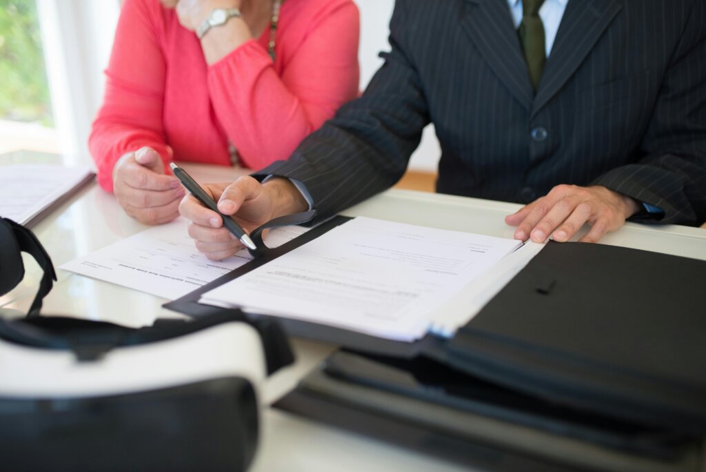 Close-up of two people reviewing and signing documents at a table, with one person holding a pen, indicating a formal agreement or transaction.