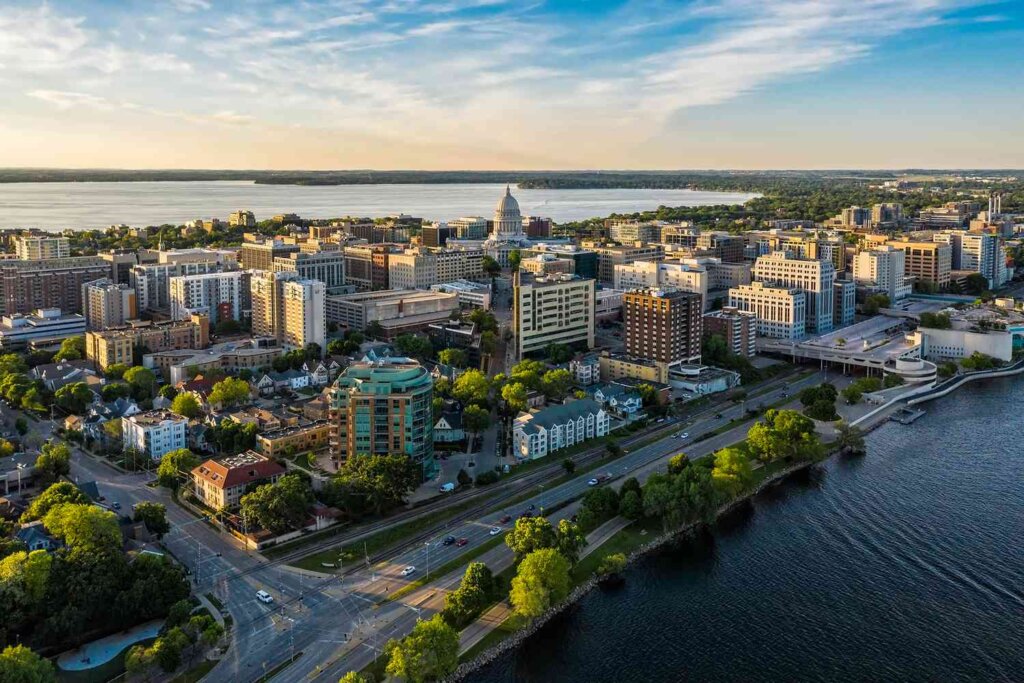 A panoramic aerial view of Madison, Wisconsin, capturing the city’s skyline along the water’s edge, including residential areas and the bustling downtown.