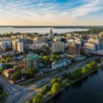 A panoramic aerial view of Madison, Wisconsin, capturing the city’s skyline along the water’s edge, including residential areas and the bustling downtown.