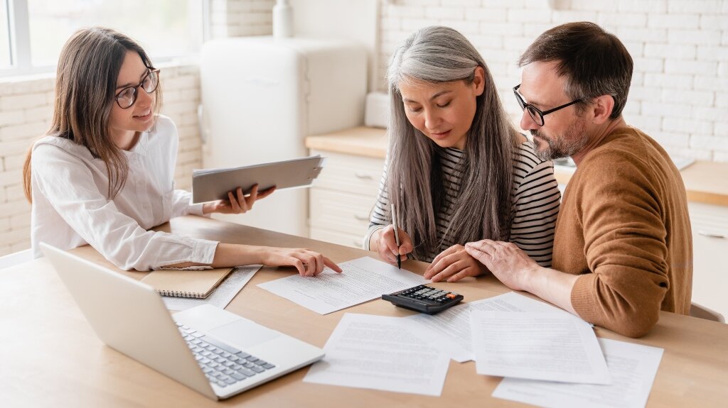 Couple reviewing documents with a female advisor at a table, using a calculator and laptop.