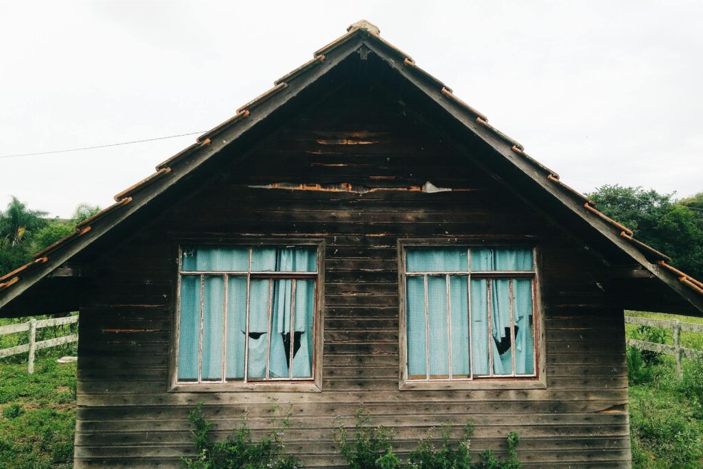Old wooden house with broken windows and blue curtains.