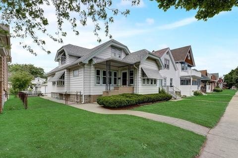cozy, single-story craftsman-style home with a spacious wrap-around porch, well-maintained greenery, and a manicured lawn. The house has large windows, a broad entryway, and is set against a backdrop of neighboring homes on a quiet residential street.
