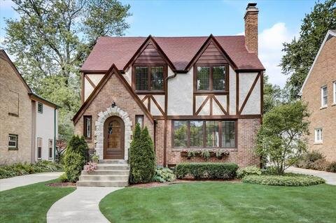 A beautiful Tudor-style house with a red pitched roof, white and brick exterior, and decorative wood paneling. The neatly manicured lawn and pathway leading to the arched wooden front door add a classic and elegant touch to the property.