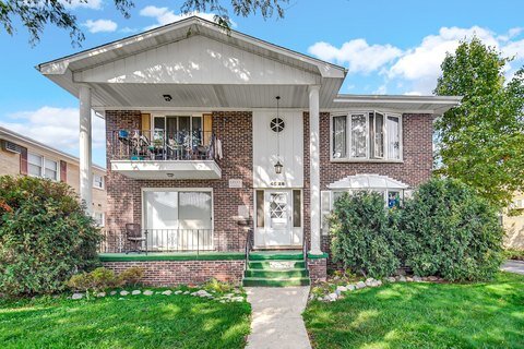 A luxurious brick house with large windows, multiple levels, and an expansive backyard featuring a well-maintained lawn, flower beds, and a patio. A swimming pool and lush greenery surround the property, creating a sophisticated yet inviting outdoor space.