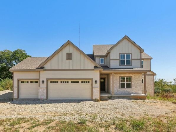 A single-story brick ranch-style home with a well-manicured lawn and bushes, featuring a welcoming front entrance. The home is set in a large open yard under a bright blue sky.