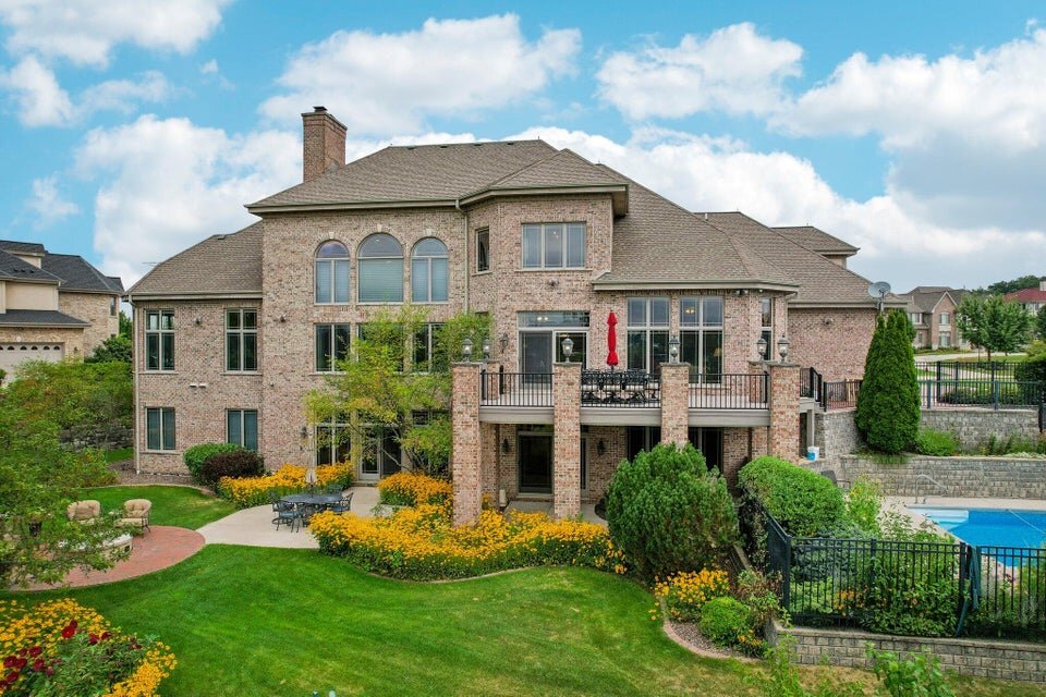 A two-story brick house with a green-painted staircase and a covered front porch. It has balconies on the second floor, large windows, and a neatly trimmed lawn, providing a comfortable and classic residential appearance.