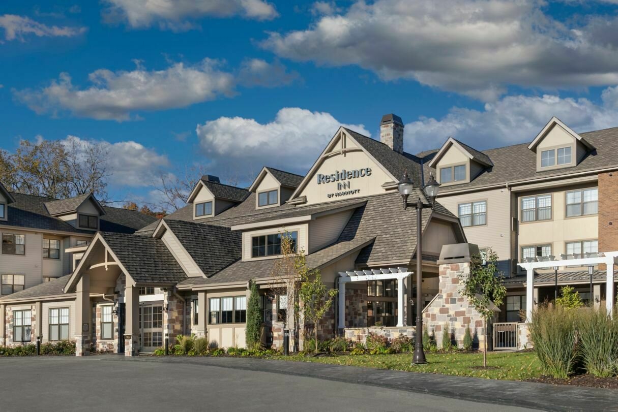 Exterior view of the Residence Inn by Marriott building, showcasing a charming, lodge-style hotel with pitched roofs and stone accents, set against a bright blue sky and fluffy clouds.
