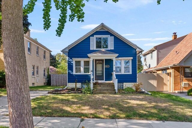 A charming, single-family home with bright blue siding and white trim. The house has a small front porch and a neatly maintained front yard, set on a suburban street with neighboring homes nearby.