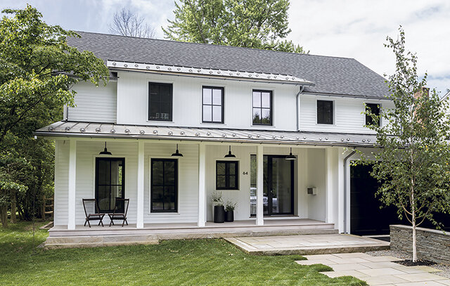 A contemporary white two-story house with black-framed windows, black hanging lights on the front porch, and a neatly landscaped green lawn. The house features a simple yet elegant facade with a clean aesthetic.