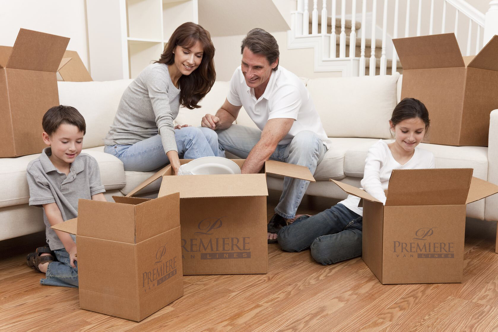 Happy family unpacking cardboard boxes in their new home. The mother, father, son, and daughter are sitting on the living room floor, smiling as they take items out of the boxes, surrounded by moving supplies.