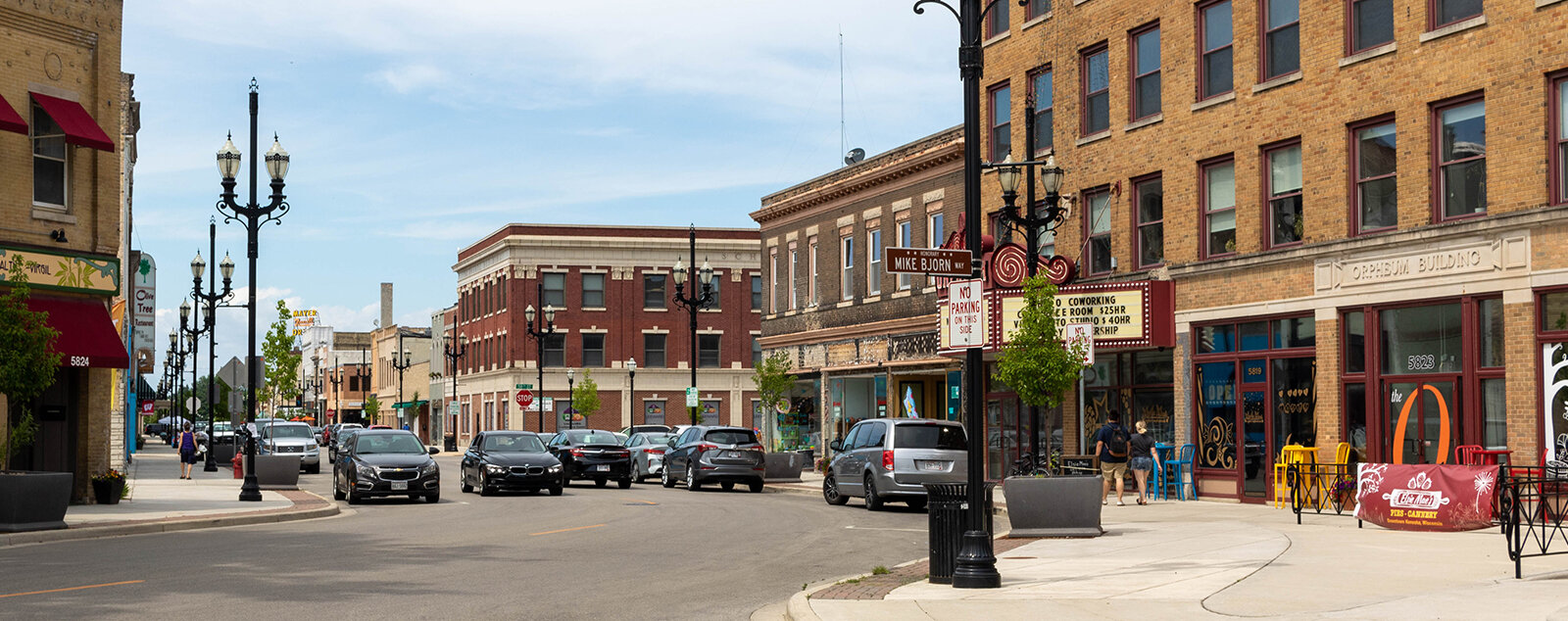 A bustling downtown street lined with historic brick buildings, local businesses, and parked cars. The area features a classic American main street feel, with pedestrians and vibrant storefronts creating a lively atmosphere.