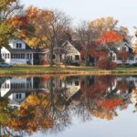 Autumn scene with waterfront homes and colorful tree reflections.