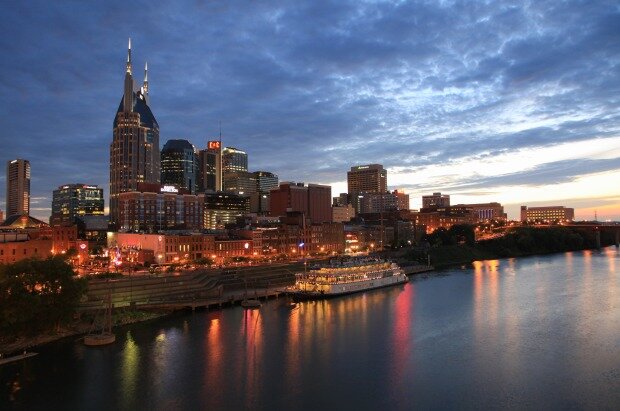 A vibrant city skyline along the river, lit up at night with skyscrapers and boats reflecting off the water, depicting a lively metropolitan scene.