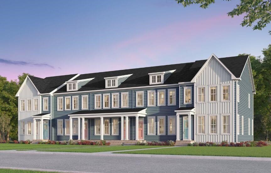A row of newly constructed townhouses in a blue and white color scheme. The multi-story homes feature large windows, stylish siding, and a front porch. The sky is transitioning into dusk with a soft pink hue.