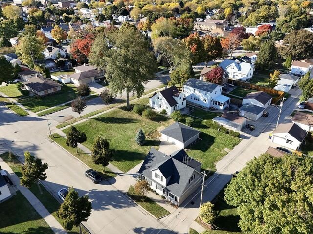 Aerial view of a quaint suburban neighborhood during autumn. Tree-lined streets are surrounded by charming homes, with colorful foliage adding vibrant hues to the landscape.