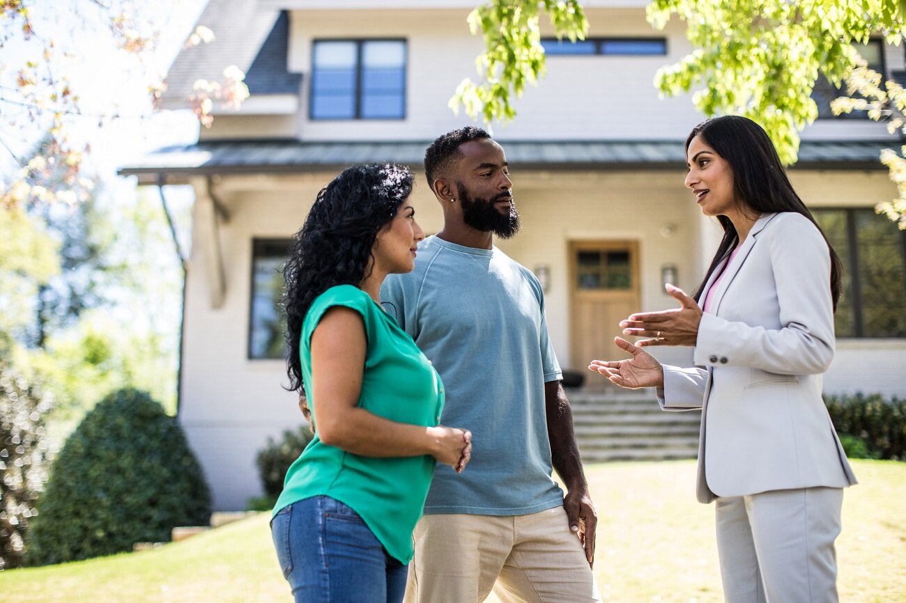 A real estate agent engaging in a discussion with a couple outside a residential property, signifying a home viewing or consultation session.