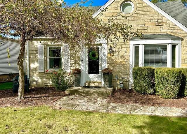 A charming single-story home with a stone facade and a small arched window. The front yard is neatly landscaped with bushes, and a small tree overhangs the front pathway leading to a white front door. The exterior has a cozy and rustic look, perfect for a suburban setting.