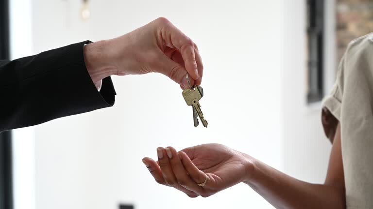 Close-up shot of a real estate agent handing over keys to a new homeowner. The agent's hand, dressed in a suit, extends the keys, while the new homeowner’s open hand receives them, signifying the finalization of a property sale or rental agreement.