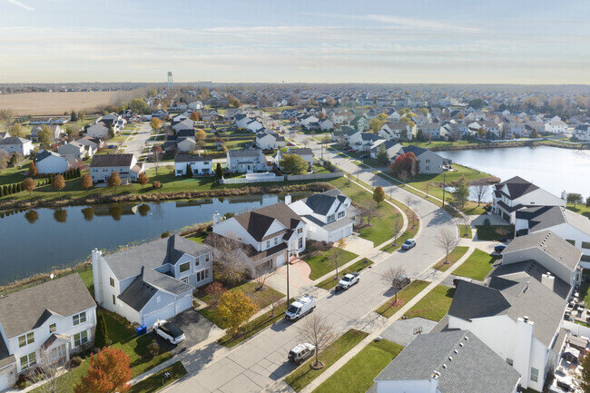 Aerial view of a beautiful residential neighborhood, showcasing well-maintained homes, a peaceful lake, and neatly arranged streets. The image captures the tranquility and orderliness of suburban living, highlighting community planning and serene surroundings.