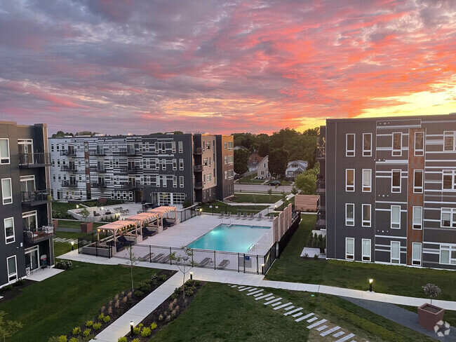 Modern apartment complex featuring a courtyard with a large swimming pool, surrounded by well-maintained landscaping and set against a vibrant sunset sky, emphasizing a contemporary urban lifestyle.