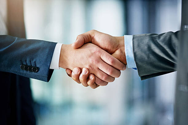 Close-up of two businessmen shaking hands, both dressed in formal suits, symbolizing a successful agreement or business deal.