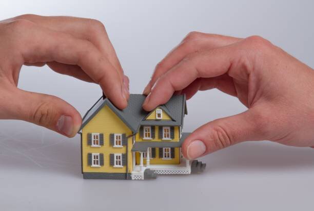 Two hands holding opposite sides of a small model house, symbolizing property division or a real estate transaction.
