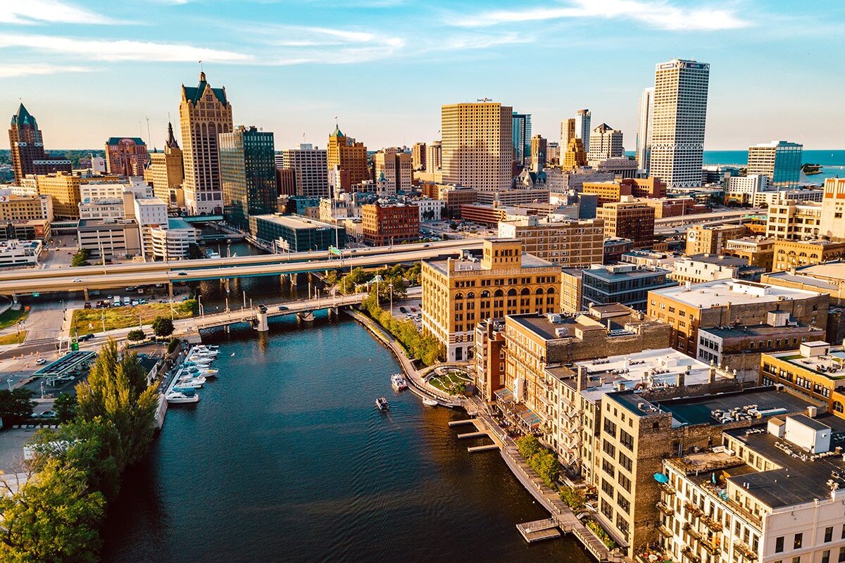 A high-angle view of downtown area, featuring tall buildings along the riverfront, highlighting the city’s vibrant architecture and waterfront beauty under a bright, blue sky.