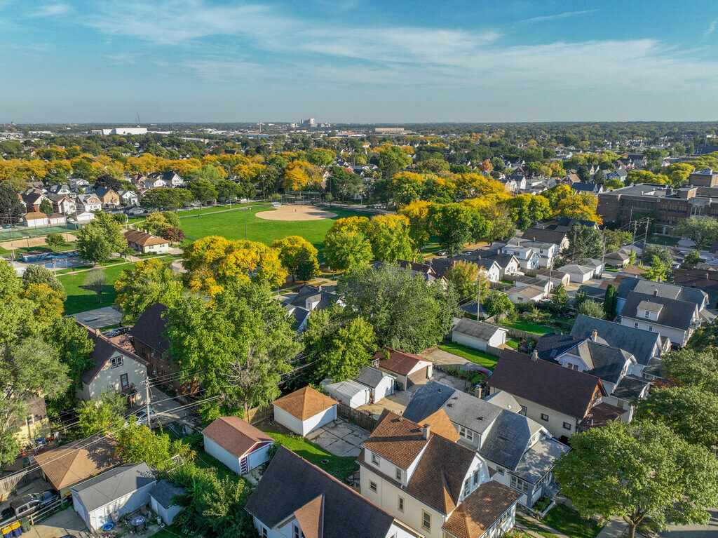 Aerial view of a neighborhood park and surrounding houses with vibrant green and yellow trees, representing a serene residential area with neatly arranged homes and ample greenery.