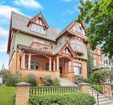 A stunning, multi-story Victorian-style home with green and red accents, featuring intricate woodwork, gabled roofs, and a large wrap-around porch. The well-maintained garden and wrought-iron fence add to the historic charm of this architectural gem.