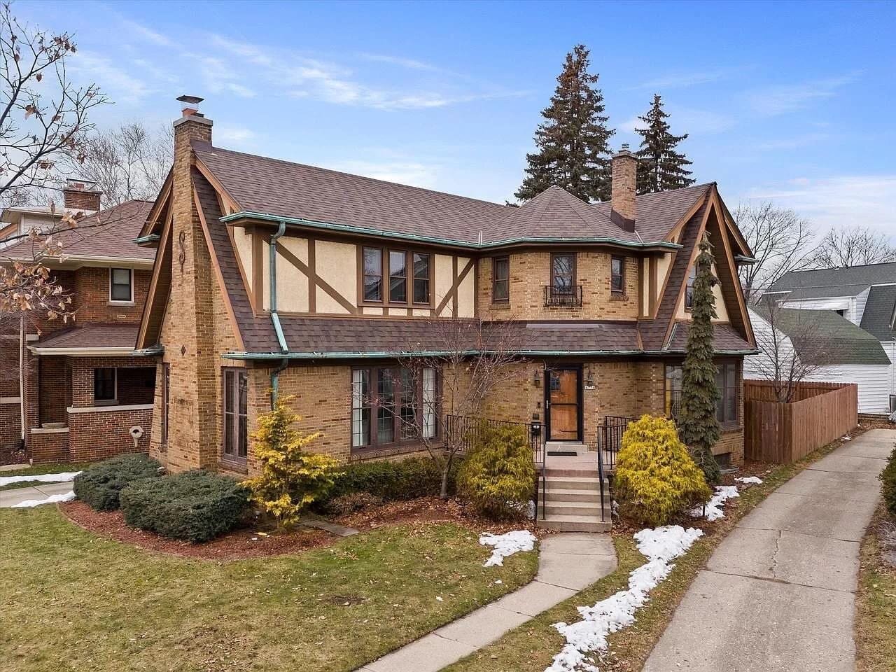 A classic Tudor-style brick home with a steep, pitched roof and ornate wooden trim, surrounded by a winter landscape. The house features tall, narrow windows and a central chimney, exuding charm and historic character.
