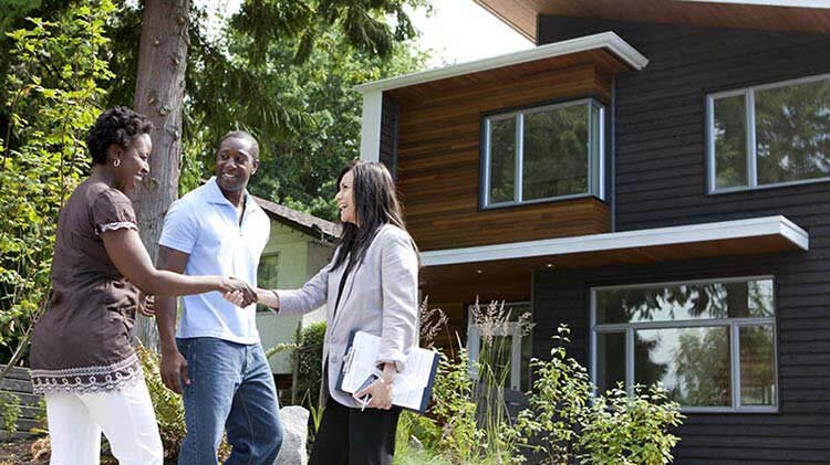 Real estate agent shaking hands with a couple in front of a modern house.