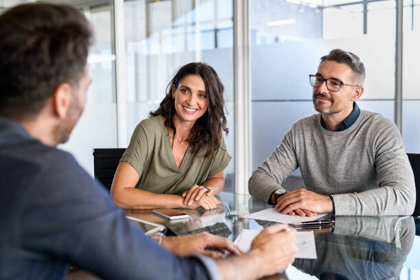 Smiling couple discussing a contract with a professional at a glass-top table.