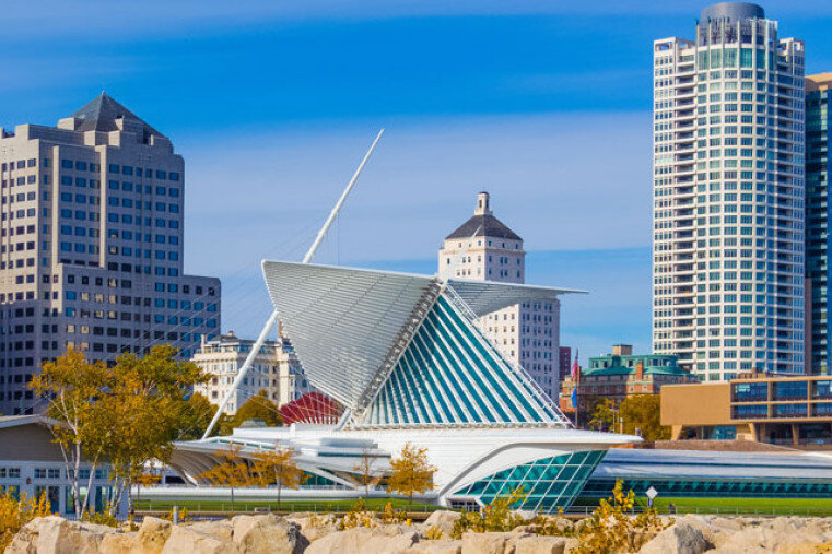 View of the Milwaukee Art Museum with its iconic, sail-like architecture against the backdrop of downtown Milwaukee. The modern building, with its striking white wings, contrasts beautifully with the surrounding skyscrapers and clear blue sky.