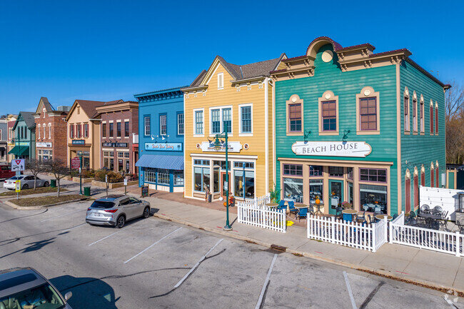 Colorful storefronts in a small-town setting with a clear blue sky, featuring vibrant yellow, green, and blue buildings, each housing unique shops, and a few parked cars along the street.