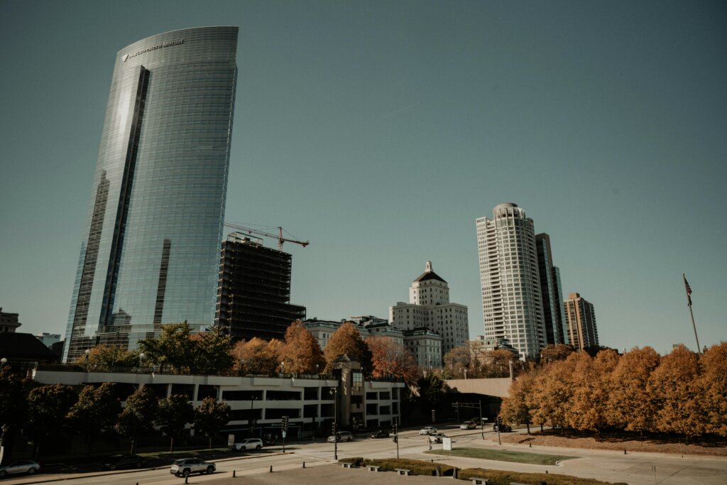 Milwaukee city skyline with tall modern buildings and autumn trees under a clear sky, showcasing urban architecture.