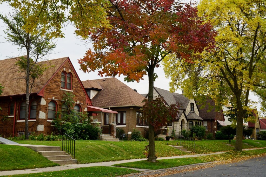 Residential street in Milwaukee with brick houses and trees displaying autumn colors, creating a cozy neighborhood vibe.
