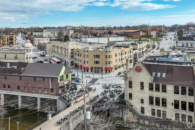 A scenic aerial view of a historic downtown area with stone and brick buildings, a bridge over a river, and outdoor dining spaces on a sunny day.