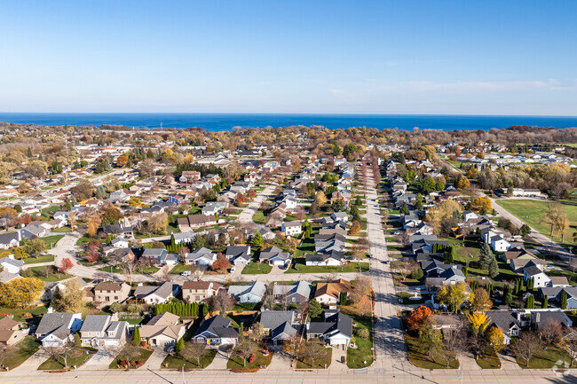 Aerial view of a suburban neighborhood with houses, tree-lined streets, and a scenic body of water in the background.