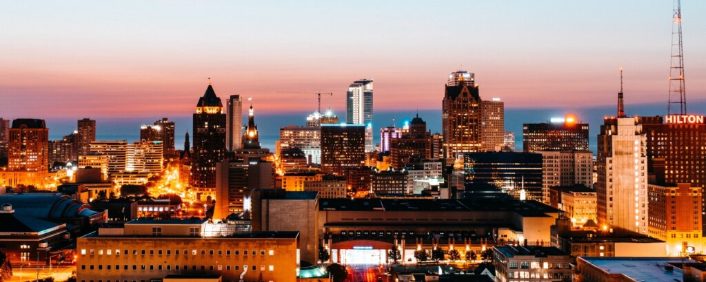 Milwaukee city skyline at dusk, with buildings lit up and a view of the horizon.
