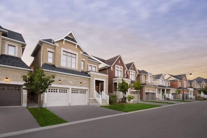 Modern suburban street in Brookfield featuring a row of elegant two-story homes with brick and stone facades, well-maintained lawns, and garages at sunset.