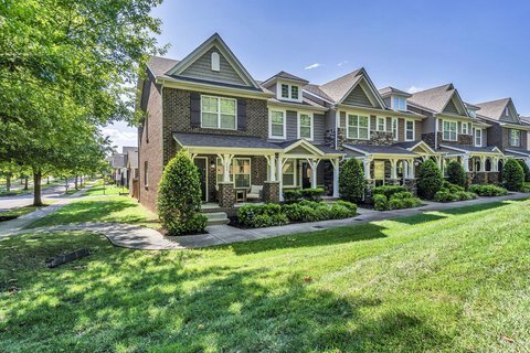 A row of modern townhouses with brick and siding exteriors, surrounded by lush green lawns and mature trees on a sunny day.