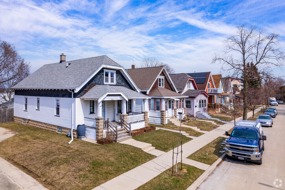 A row of charming suburban houses with pitched roofs in Bay View, Milwaukee, WI, on a sunny day, with parked cars lining the quiet residential street.