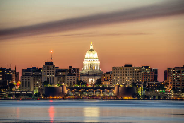 A scenic view of the Wisconsin State Capitol in Madison, illuminated at sunset with the city skyline in the background.